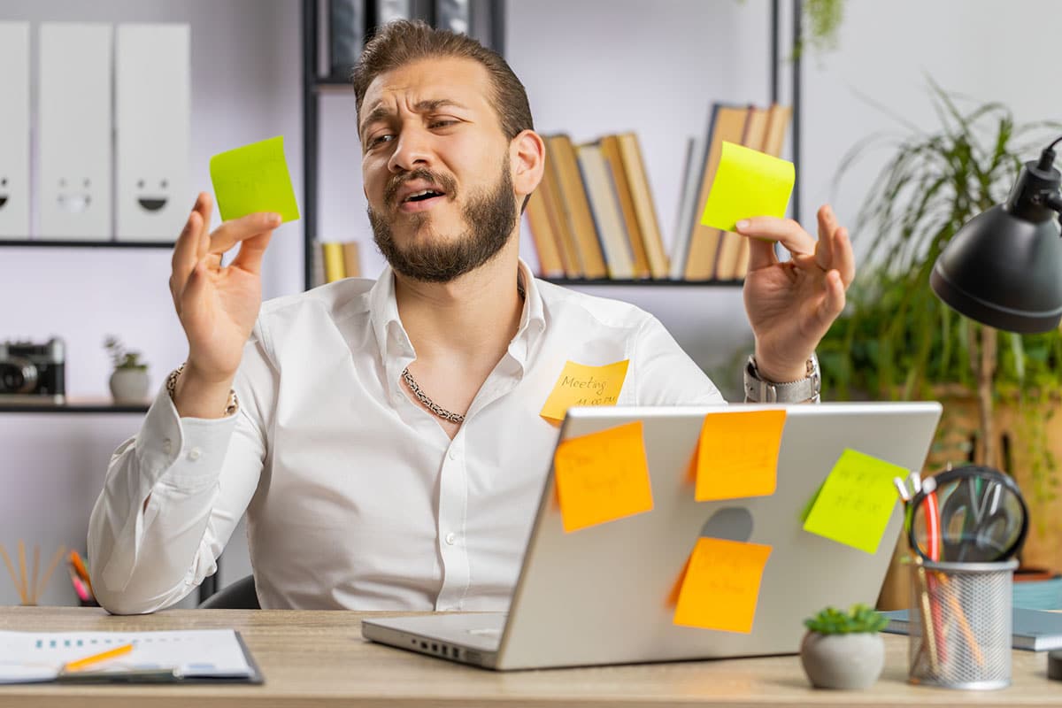 business man sits at desk with post it notes all over his desk and laptop indicating information overload during induction training