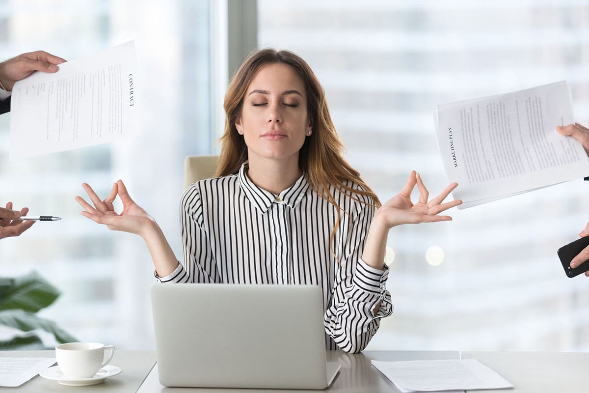 business woman meditates during high stress situation with colleagues asking for multiple work items