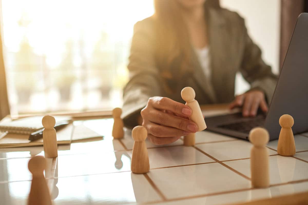 business woman with laptop in front of her rearranges wooden figures on table indicating change management