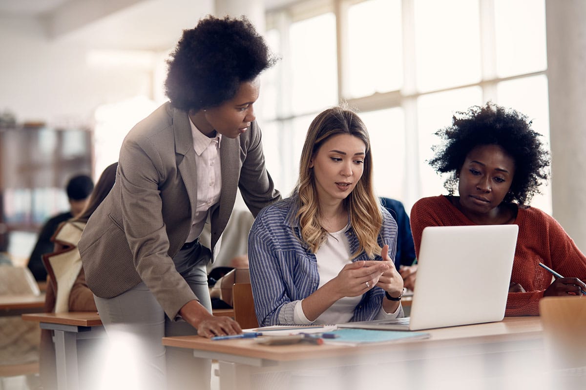 female teacher helps college students working on laptop and taking notes