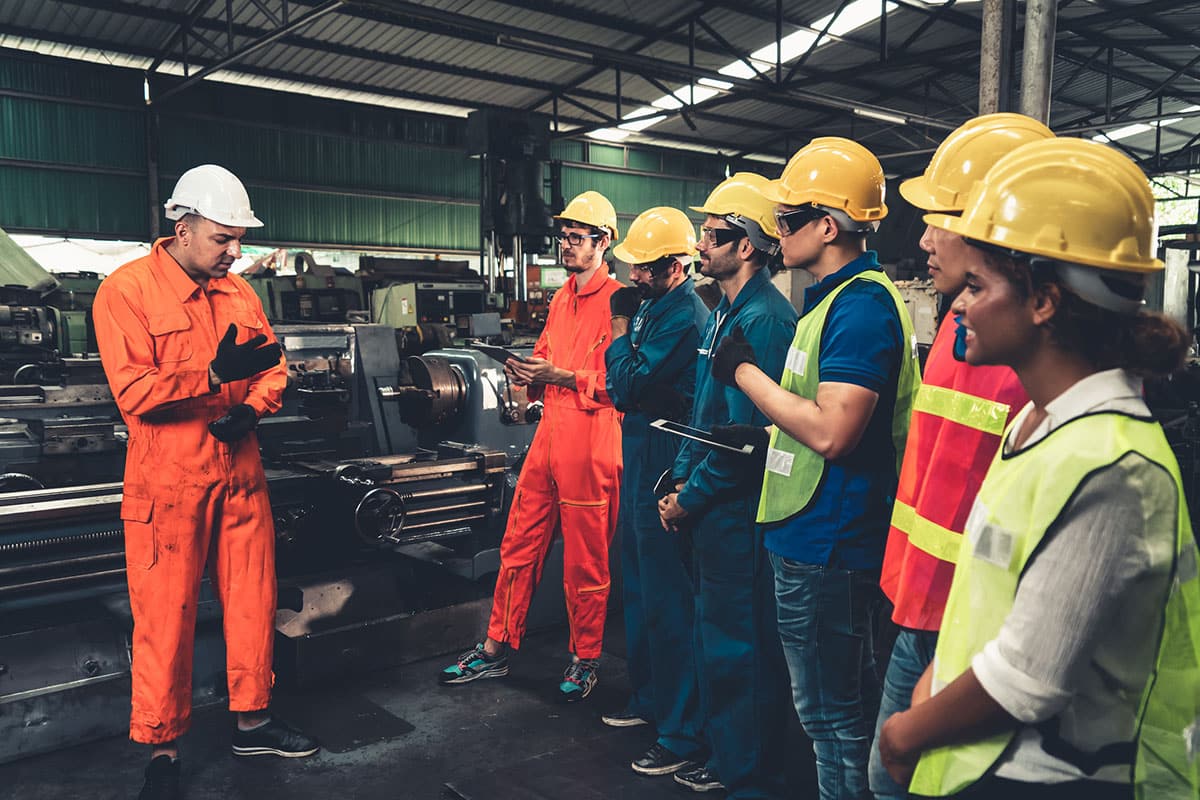 group of new employees wearing safety hats, safety vests and overalls go through health and safety induction training