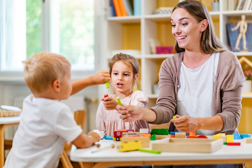 Kindergarten teacher playing together with children preschool classroom