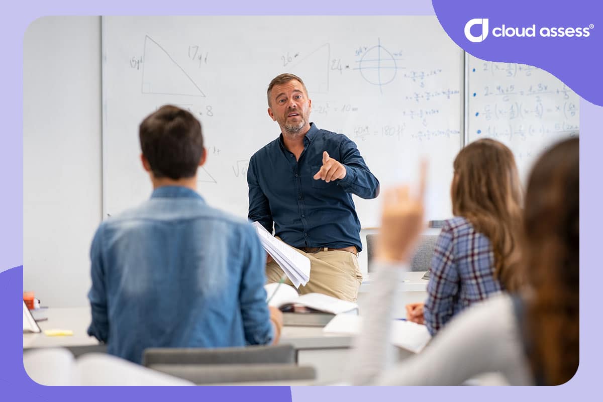 lecturer with equations on whiteboard behind him answers individuals question