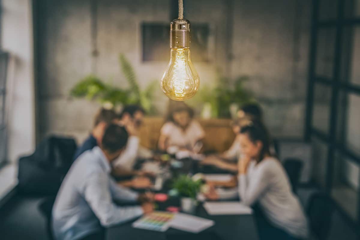 lightbulb in focus with team meeting in blurred background highlighting innovation