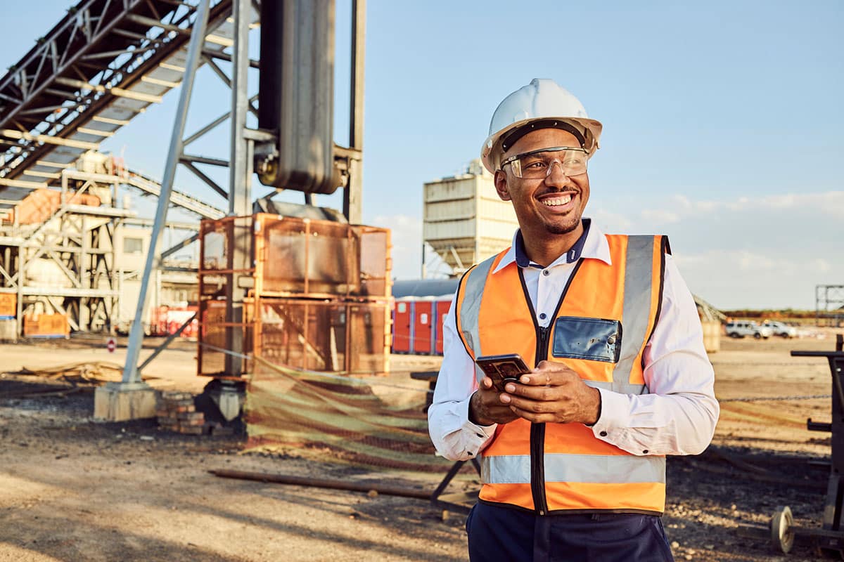 man wearing safety helmet and vest accessing induction training on cellphone