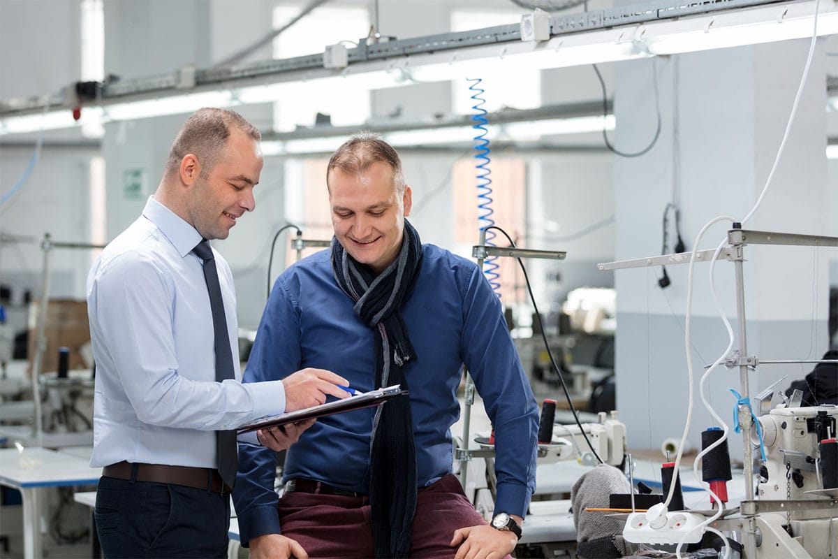 men look at checklist together with machinery in the background as part of succession planning