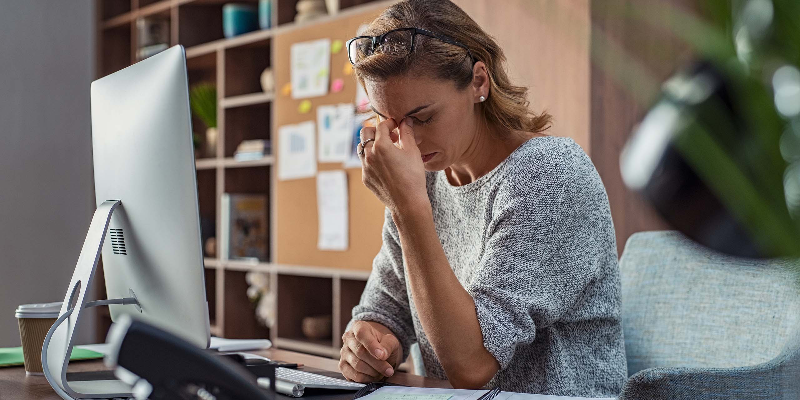 business woman works at computer and holds head in frustration with lms