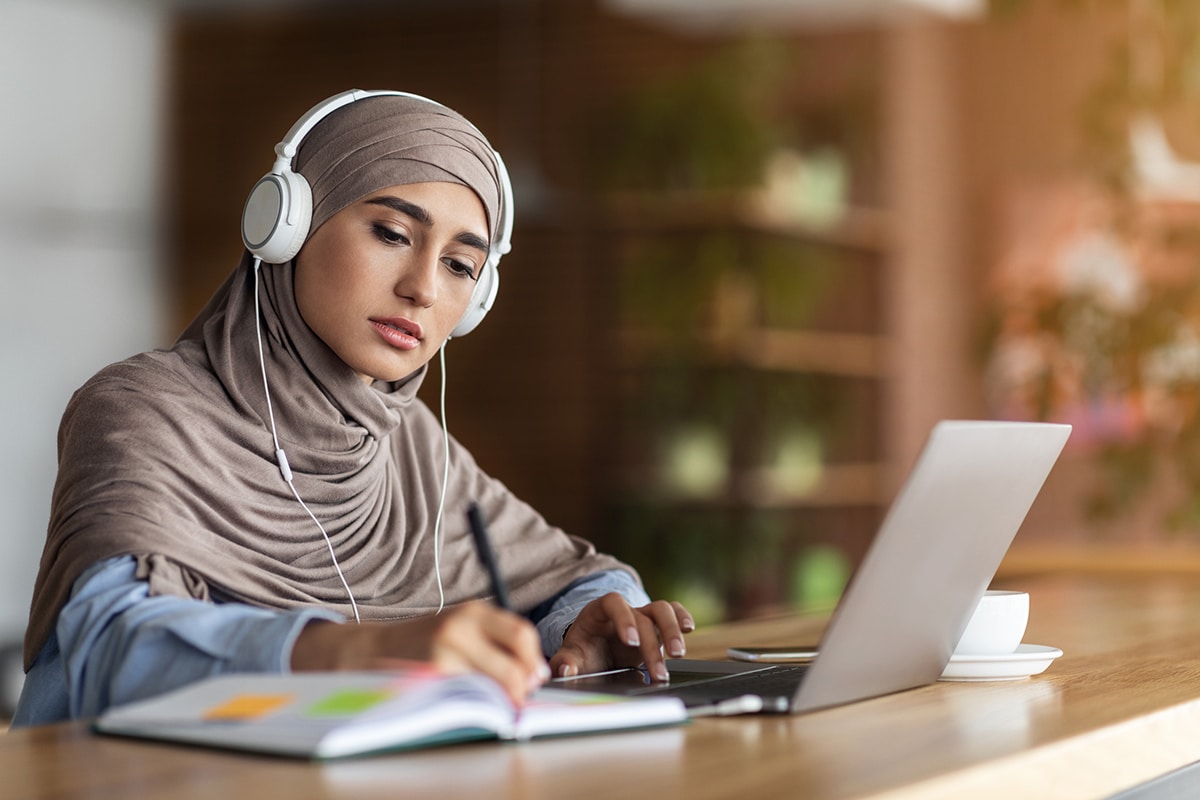 student highlights book and makes notes while taking a microlearning lesson on her laptop in a coffee shop