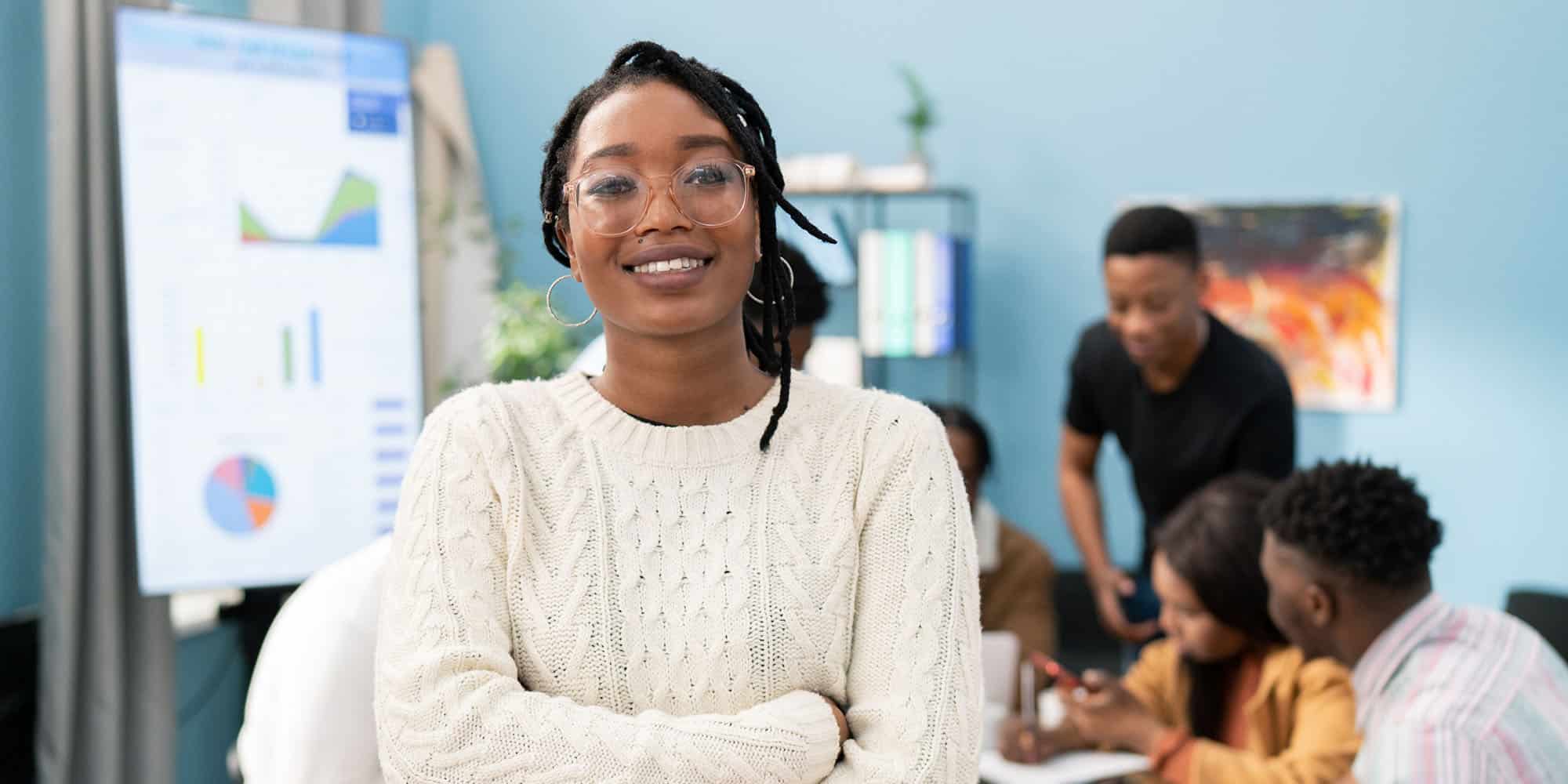 woman in focus with group of students working behind her and data projected on a smart screen
