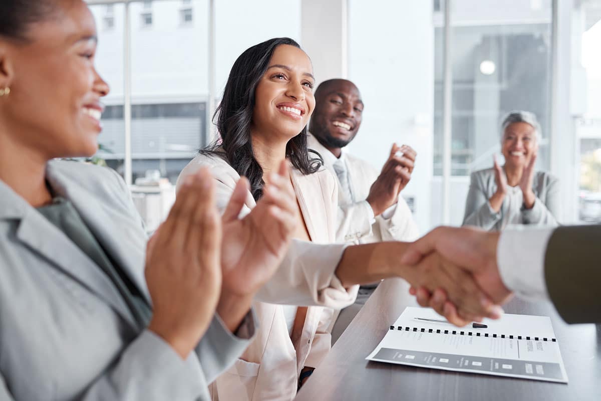 team clap while business woman shakes hands with company owner indicating career advancement