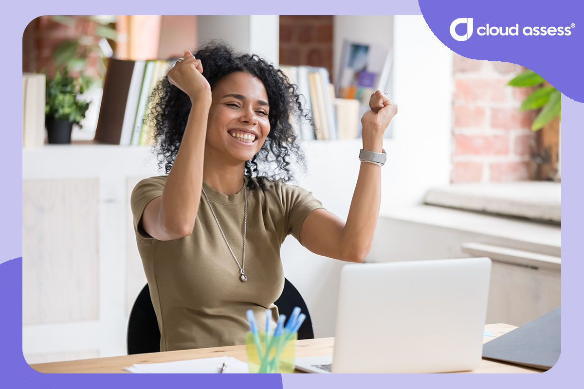 woman celebrates while sitting in front of laptop in office